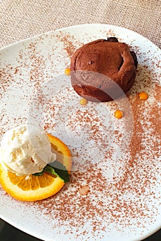 Close up of hot melting chocolate cake dessert and scoop of vanilla ice cream on orange slice on white plate. Chocolate fondant