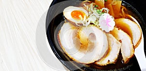 Close up hot ramen noodle soup, pork sliced, egg yolk and white spoon in black bowl on wooden table