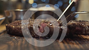 Close-up of hot tasty steak cut with knife on a wooden board. Action. Medium Rare degree of steak doneness