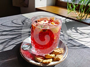 Close-up of a hot tea mug with grenadine and fruits next to cookies on a table in a cafe in bright sunlight