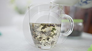 Close-up hot water pouring in transparent cup with tea leaves. Brewing of healthful detox organic drink indoors.