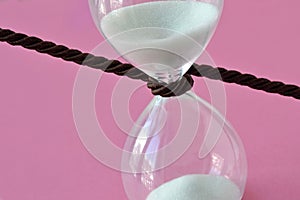 Close-up of hourglass with a cord around it on pink background - Stop the time concept