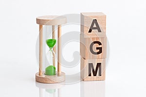 Close-up of an hourglass next to wooden blocks with the text AGM. AGM - Annual general meeting