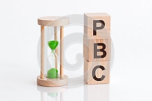 Close-up of an hourglass next to wooden blocks with the text PBC