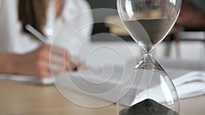 close-up hourglass. Silhouette woman reading a book and write conspectus on a blurred background 4k