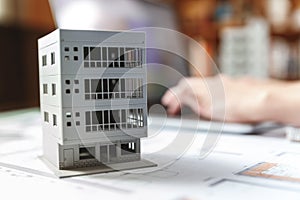 Close up of a house model standing over apartment plans in front of a laptop in a construction bureau