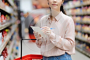 Close up of housewife choosing groceries in supermarket. Young woman holding list of products is shopping. Close up. In