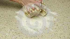 Close-up of housewife's hands kneading and crumpling dough on bright kitchen table sprinkled with white wheat flour