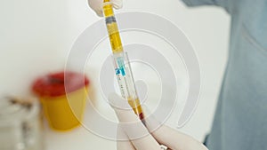 A close-up of how a doctor collects plasma from a test tube into a syringe.