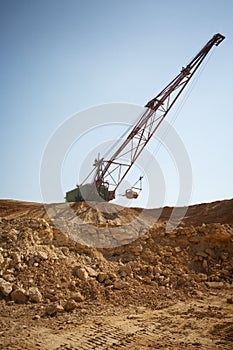 Close-up of a huge metal mobile crane on a blue sky background. An industrial moving machine in the foundation pit. Copy