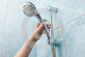 Close-up of human hand adjusts holder shower head with hose.