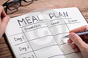Human Hand Filling Meal Plan In Notebook photo