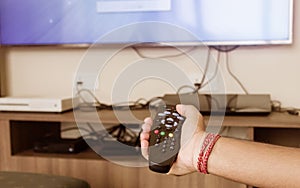 Close up of Human Hand holding a Remote control and pointed towards a TV screen for changing or zapping channels. Modern