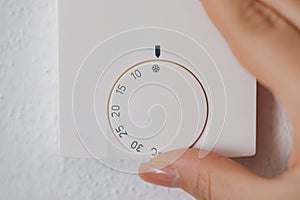 Close-up of human hand turns off the heating at home. Central Heating thermostat control dial adjustment. Woman turning