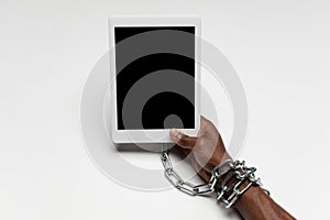 Close up of human hand using tablet with blank black screen. Tied with chain, addiction