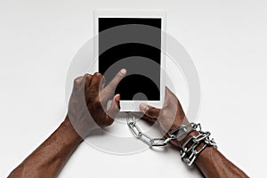 Close up of human hand using tablet with blank black screen. Tied with chain, addiction