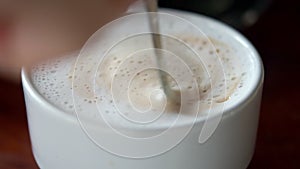 Close up of human hand using teaspoon stirring hot coffee in white ceramic cup.