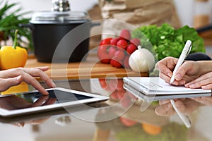 Close-up of human hands are gesticulate over a tablet in the kitchen. Friends having fun while choosing menu or makin