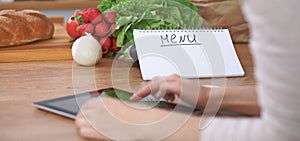 Close-up of human hands are gesticulate over a tablet in the kitchen. Women choosing menu or making online shopping. So
