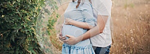 Close up of human hands holding pregnant belly, closeup happy family awaiting baby, standing on green grass, body part, young fami