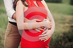 Close up of human hands holding pregnant belly, closeup happy family awaiting baby, standing on green grass, body part, young fami