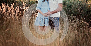 Close up of human hands holding pregnant belly, closeup happy family awaiting baby, standing on green grass, body part, young fami