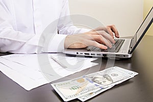 close-up of human hands typing on a computer keyboard. in the foreground are dollar bills