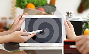 Close-up of human hands using tablet or touch pad. Two women in kitchen. Cooking, friendship or online shopping concepts