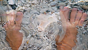 Close-up. human legs in water. under the clear water of the Aegean Sea, small multi-colored pebbles are visible