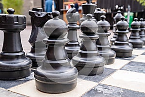 Close up of human sized black chess pieces with pawns in front