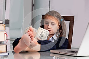 Close up humorous portrait of happy cute young business girl counts money profit with bare feet on the table. Selective focus on