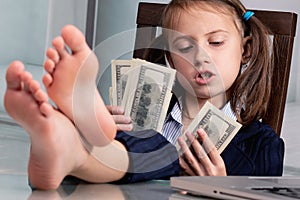 Close up humorous portrait of happy cute young business girl counts US Dollar money profit with bare feet on the table. Selective