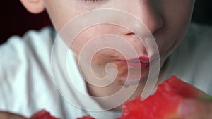 Close-up of a hungry Caucasian boy eating a ripe juicy watermelon, the child`s lips are wet from the juice of a delicious watermel