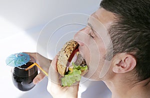 Close-up. A hungry young man eats a big hamburger sandwich with beef, tomatoes, onions, sauce, cheese, lettuce and a sesame bun