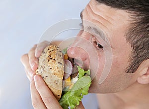 Close-up. A hungry young man eats a big hamburger sandwich with beef, tomatoes, onions, sauce, cheese, lettuce and a sesame bun