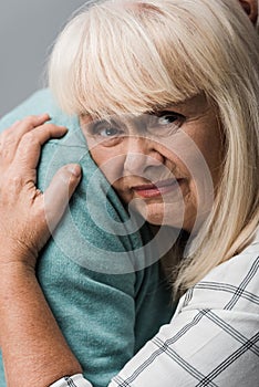 close up of husband hugging sad retired wife with grey hair isolated on grey.