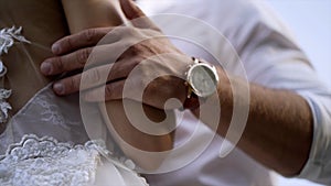 Close-up of husband`s hands hugging wife. Action. Husband gently touches his wife`s waist in white wedding dress