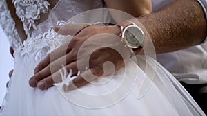 Close-up of husband`s hands hugging wife. Action. Husband gently touches his wife`s waist in white wedding dress