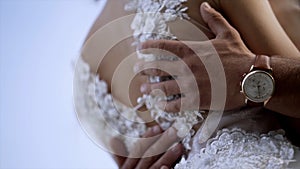 Close-up of husband`s hands hugging wife. Action. Husband gently touches his wife`s waist in white wedding dress