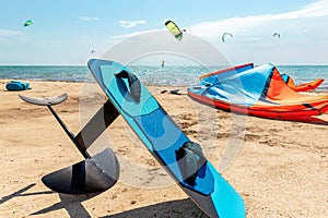 Close-up hydrofoil surf board and kite equipment on sand beach shore watersport spot on bright sunny day against sea