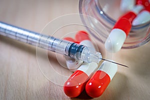 Close up of a hypodermic needle and red pills