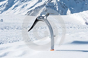 Close-up of an ice ax in the snow with snow-capped mountains in the background