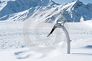 Close-up of an ice ax in the snow with snow-capped mountains in the background