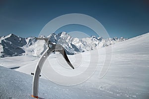 Close-up of an ice ax in the snow with snow-capped mountains in the background