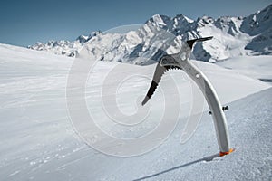 Close-up of an ice ax in the snow with snow-capped mountains in the background