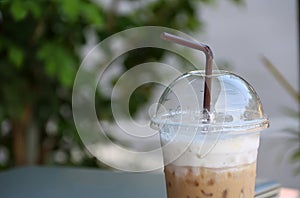 Close up ice coffee in the plastic cup with brown straw and out focus notebook.