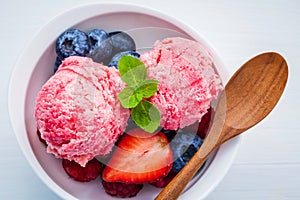 Close Up ice cream mixed berry fruits raspberry ,blueberry ,strawberry and peppermint leaves setup in white bowl on white wooden