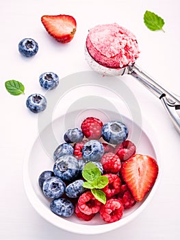 Close Up ice cream mixed berry fruits raspberry ,blueberry ,strawberry and peppermint leaves setup in white bowl on white wooden