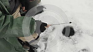 Close up of ice hole on frozen lake with fishing rod. Fisherman is fishing in ice hole. Winter fishing concept