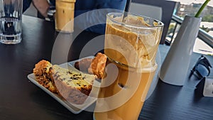 Close Up of Ice Nescafe Coffee in Unique Glass Cup with Black Straw and Fresh Cookies with Chocolate on Black Wooden Table in